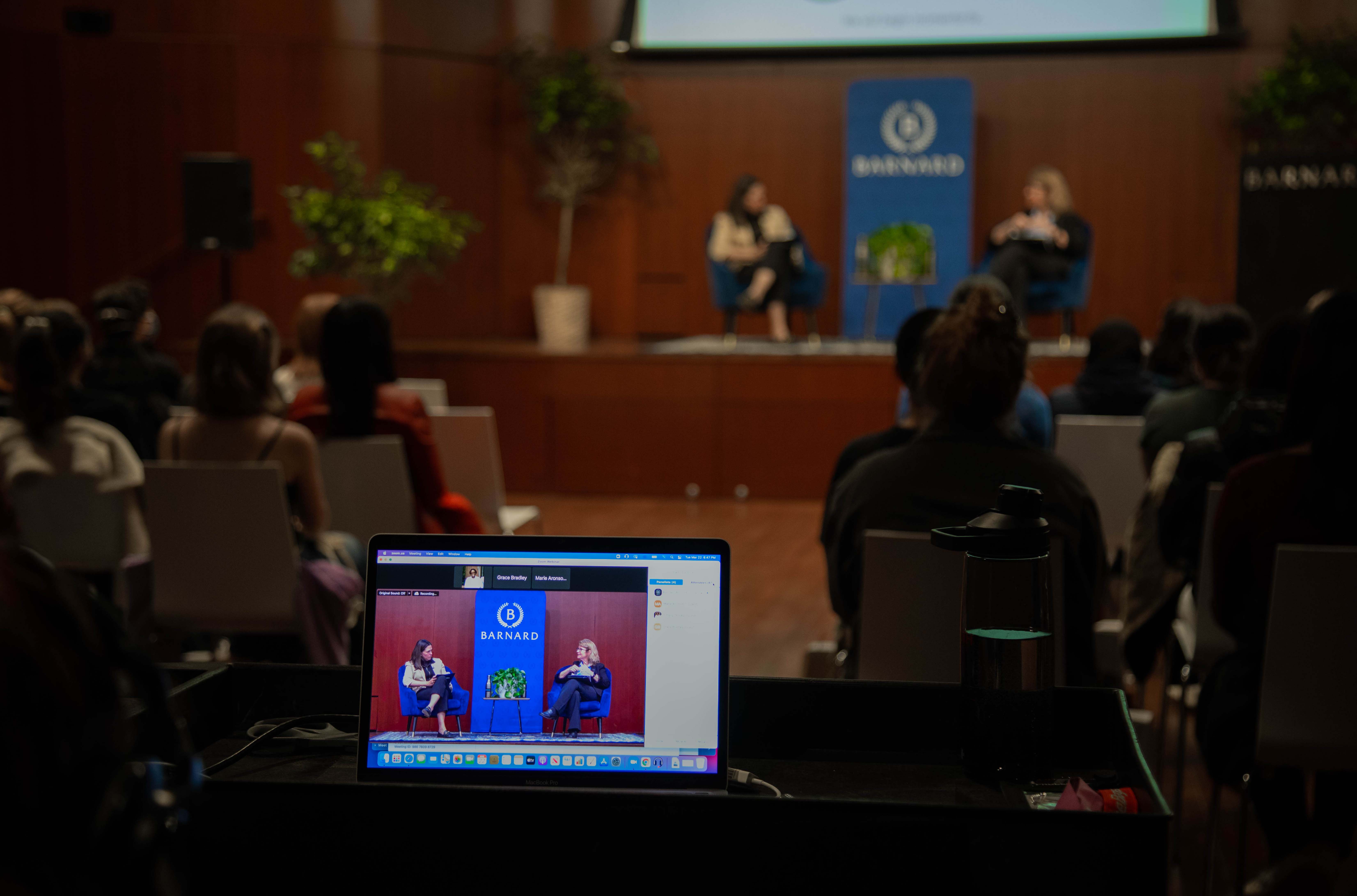 Photo shows a scene from the World of Water conference 2022. In the background, two women are seated on a stage. In the foreground, a laptop rests on a table showing a livestream of the two women.