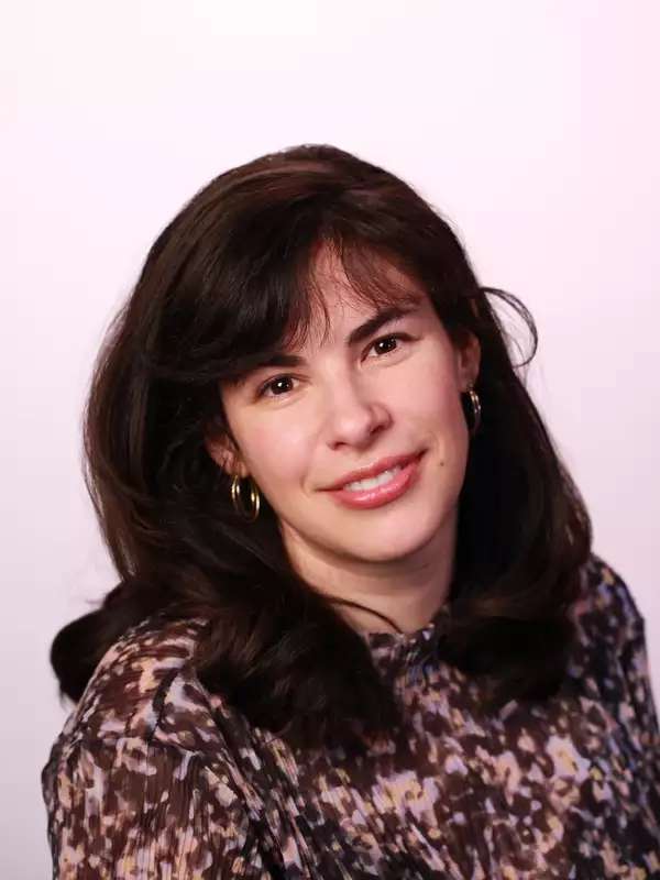 Photograph of Emily Alexander, who has brown hair and is wearing a floral shirt, smiling.